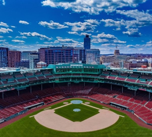 Boston Fenway Park mit roten Sitzreihen, grünem Baseballfeld und klarem blauen Himmel; sichtbare Stadionat-Architektur in der Skyline