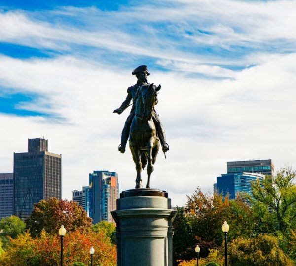 Boston bronzenes Reiterstandbild vor einer modernen Skyline, umgeben von Herbstbäumen in Orange- und Grüntönen, zentral positioniert