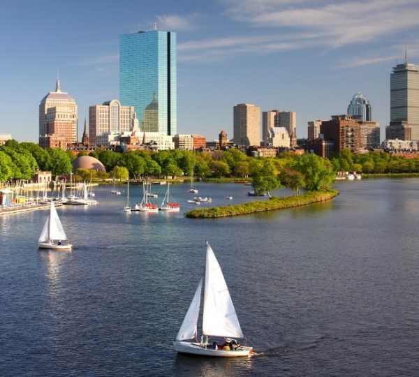 Boston Skyline am Hafen mit weißen Segelbooten, grünem Uferpark und modernen Hochhäusern im Hintergrund, ideal für Reiseinhalte über Neuengland