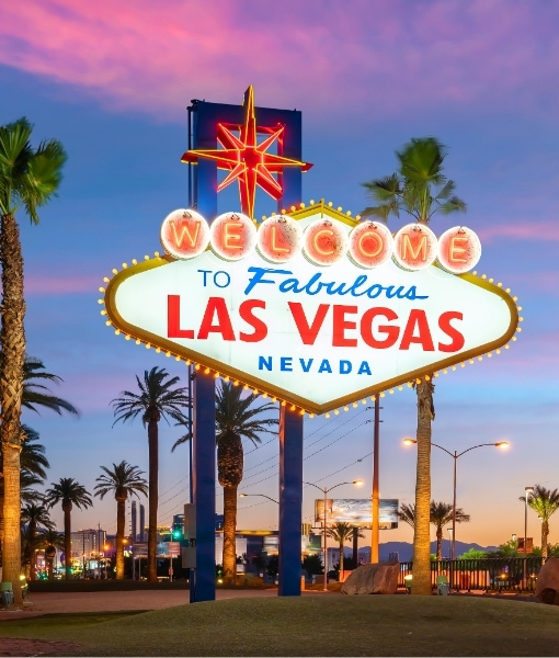 Buntes Leuchtschild „Welcome to Fabulous Las Vegas“ mit „Nevada“ am Abendhimmel, flankiert von Palmen und warmem Stadtlicht in Las Vegas.