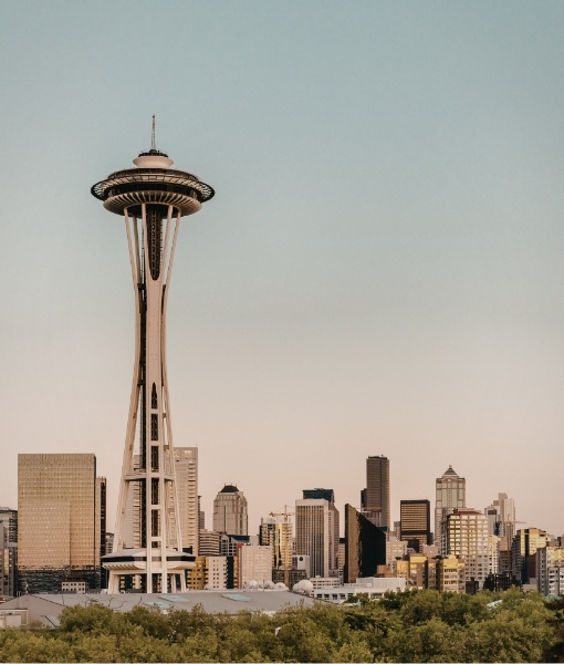 Space Needle im Pacific Nordwest mit hoher Turmkonstruktion vor städtischer Skyline, bei hellem Himmel und ruhiger Stadtansicht.