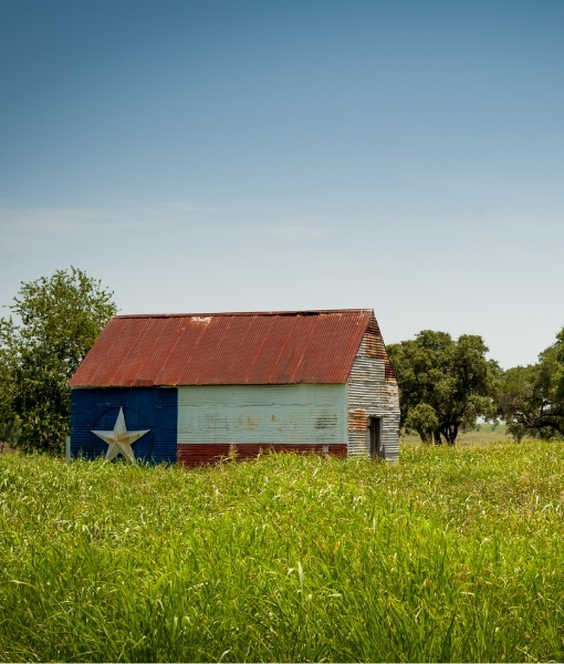 Blaue Scheune mit rotem Dach und Stern auf grüner Wiese bei Texas, Südstaaten-Stimmung und weitläufige Landschaft im Blick.