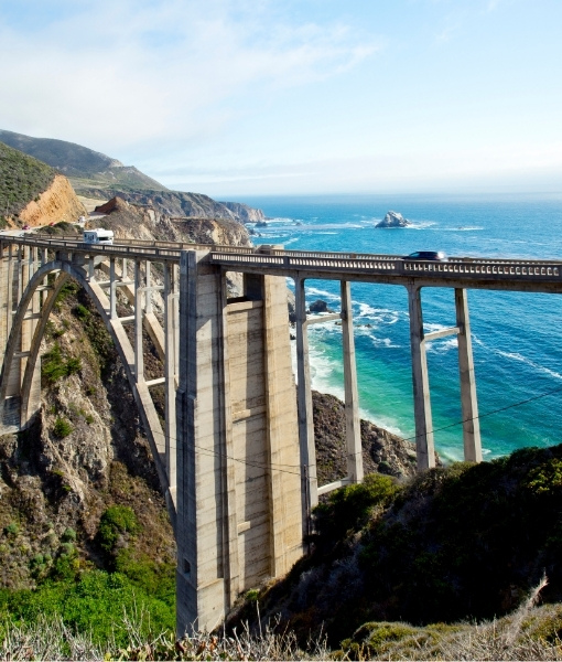 Hohe Brücke an der Westküste USA über blaues Meer, Felsenküste und steile Klippen mit Blick auf die offene See bei Tageslicht.