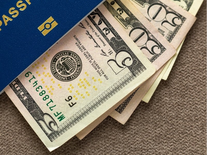 US-Dollar-Banknoten und ein blauer Reisepass liegen nebeneinander und passen zu Trinkgeld, Bargeld und Kreditkarte für das Bezahlen in den USA