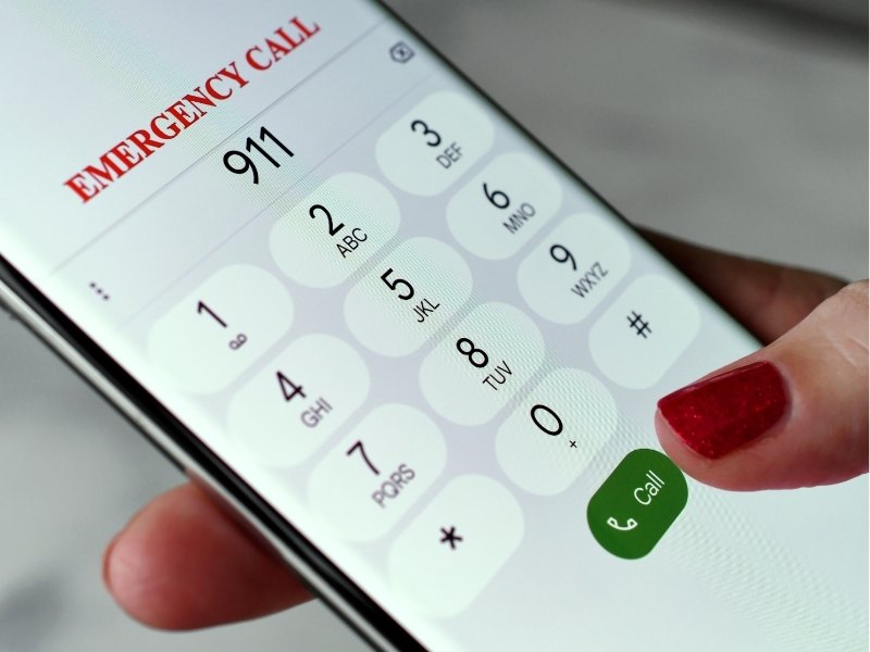 Smartphone mit Notruf-App für die USA: 911 „Emergency Call“ auf dem Ziffernblock und ein grüner Call-Button, Hand mit rotem Fingernagel.
