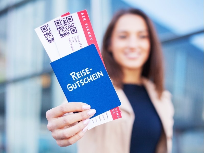 Blauer Reisegutschein mit QR-Codes und geprägtem Look, während eine Frau im Hintergrund unscharf lächelt, mit Blick auf die USA-Reisevorfreude.