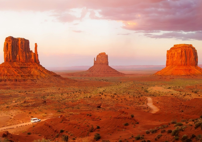 Im Südwesten USA liegt Arizona in einer weitläufigen Wüstenlandschaft mit roten Felsen und einer schmalen Straße, im warmen Abendlicht.