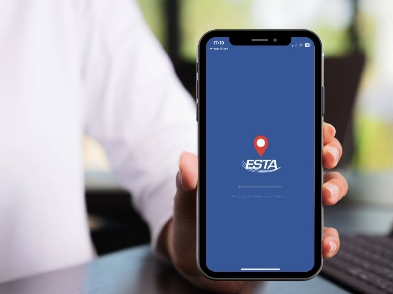 Auf einem Smartphone ist das ESTA-Logo auf blauem Bildschirm mit Standort-Pin zu sehen, während jemand das ESTA für die USA beantragt.