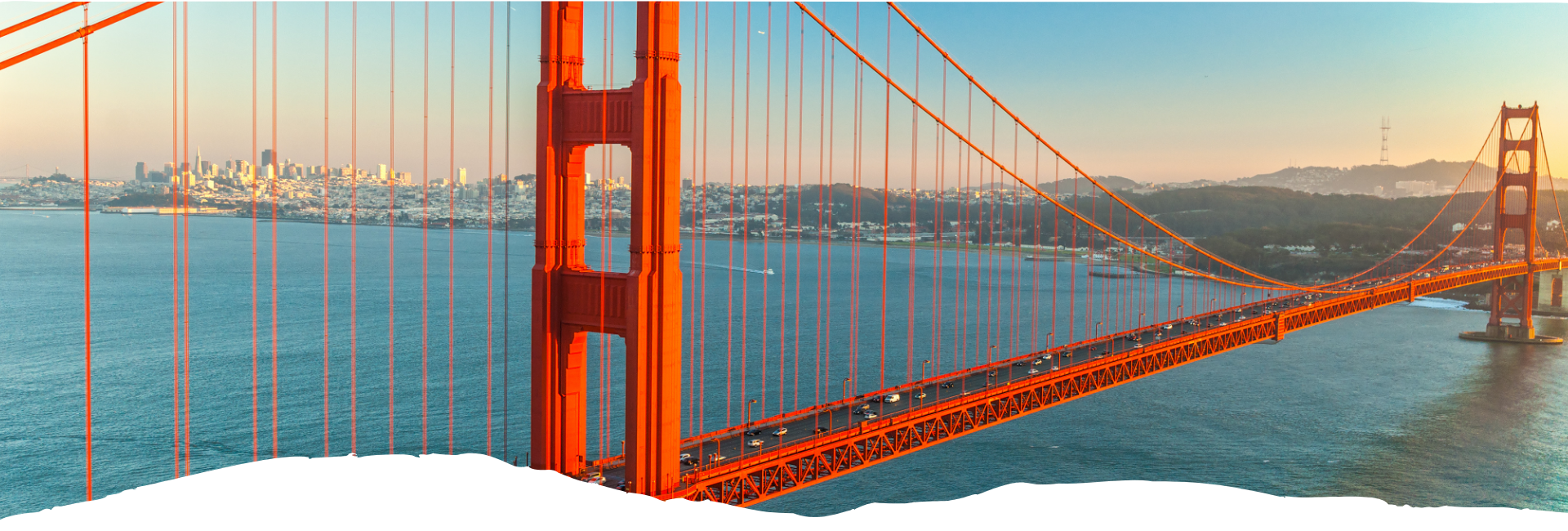 Orangefarbene Golden Gate Bridge bei Sonnenuntergang über dem Wasser, Skyline in der Ferne, passend zu Amerika-Jobs bei USA-Reisen Experte heute online.