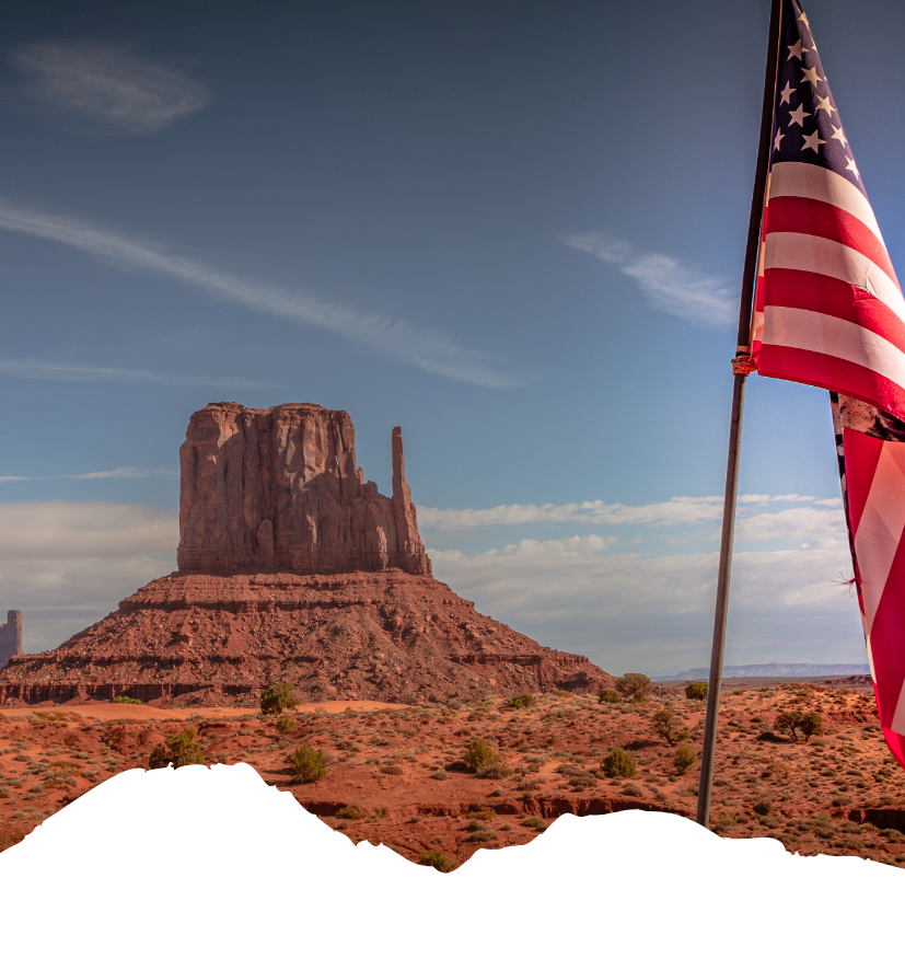 Die USA-Flagge weht vor einer roten Felslandschaft im Wüstenlicht und passt zum Planen Ihrer USA-Reise mit dem Reisebüro Bergheim.