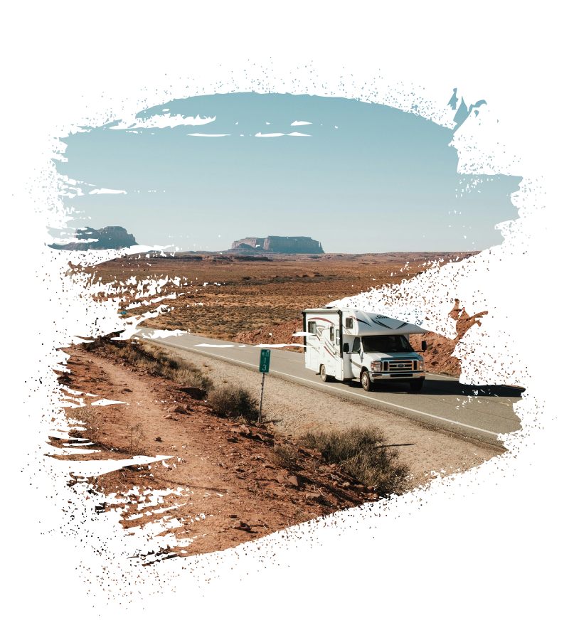Ein weißes Wohnmobil auf einer Straße durch eine sandfarbene Landschaft, im Hintergrund Felsformationen – ideal für USA Roadtrip und Route 66. USA-Reisebüro