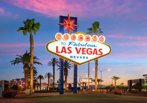 Das berühmte Welcome to Fabulous Las Vegas Nevada-Schild leuchtet bei Dämmerung zwischen Palmen vor einem violett-blauen Abendhimmel.