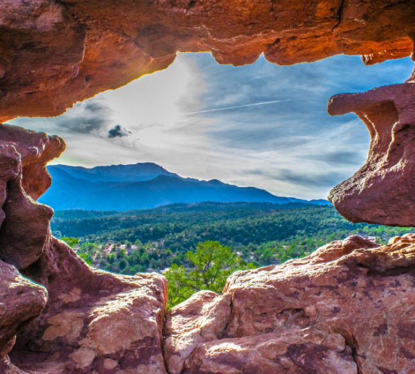 Durch ein natürliches Felsentor im Garden of the Gods reicht der Blick über grüne Wälder und die Berge Colorados.