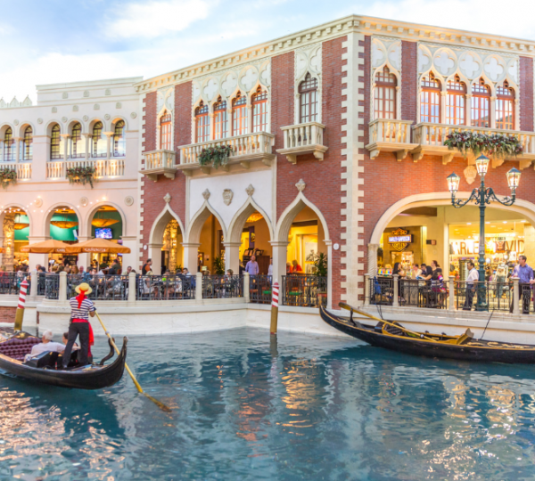 Gondoliere fahren durch eine venezianische Einkaufswelt in Las Vegas mit Arkaden, Geschäften und spiegelndem Wasser.
