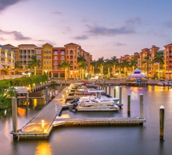 Abendliche Marina in Naples, Florida, mit beleuchteten Palmen, bunten Gebäuden und zahlreichen Booten am Wasser
