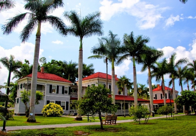 Im Edison Ford Museum in Fort Myers stehen historische Villen mit roten Dächern zwischen hohen Palmen und gepflegten Grünflächen unter blauem Himmel.