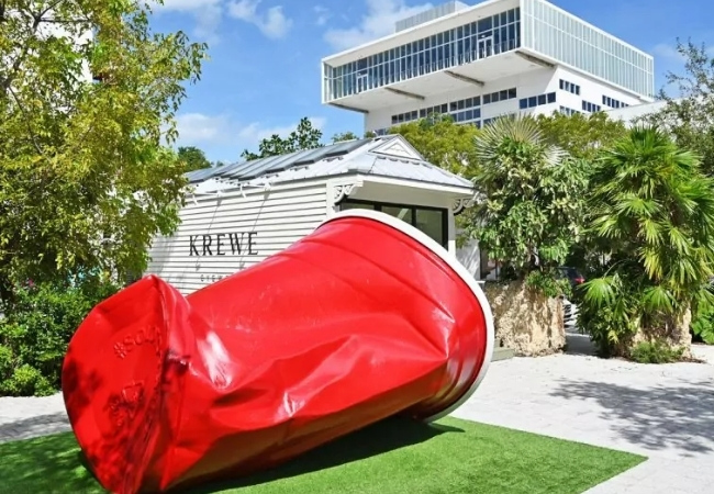Im Miami Design District liegt eine übergroße rote Dose vor einem weißen Bau mit Palmen, Rasen und blauem Himmel in sonniger Florida-Atmosphäre.