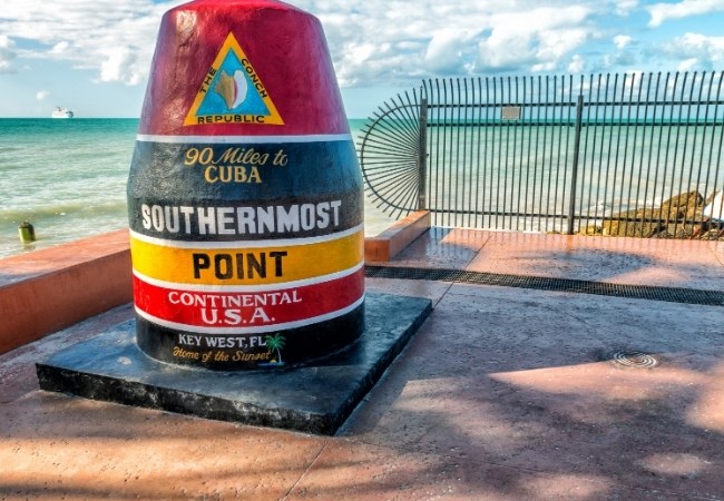 Am Southernmost Point in Key West markiert eine rot-blaue Boje den südlichsten Punkt der kontinentalen USA, mit Meer und Zaun im Hintergrund.