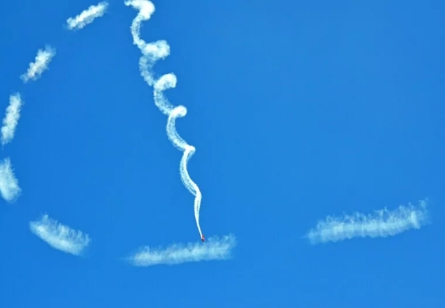 Beim Wings and Waves Airshow zieht ein kleines Kunstflugzeug eine lange weiße Rauchspur durch den klaren blauen Himmel über Florida hoch.