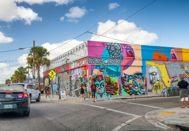 In Wynwood in Miami prägen farbige Wandgemälde, Graffiti und Palmen eine lebendige Straßenecke mit Fußgängern und Autos.