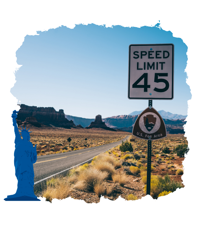 Eine einsame Wüstenstraße in den USA führt an einem Speed-Limit-Schild mit 45 vorbei, daneben steht ein U.S. Fee Area-Schild.