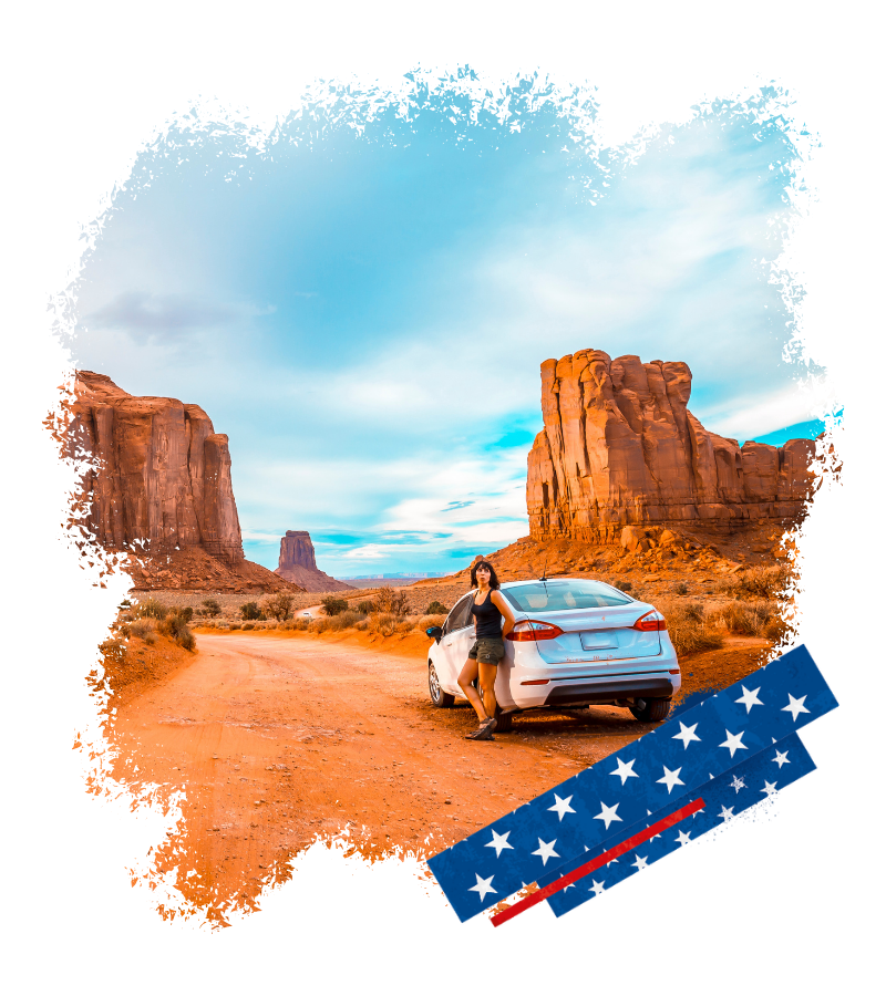 An einer staubigen Wüstenstraße lehnt eine Reisende an einem weißen Auto, umgeben von roten Felsen und weitem Himmel in den USA.
