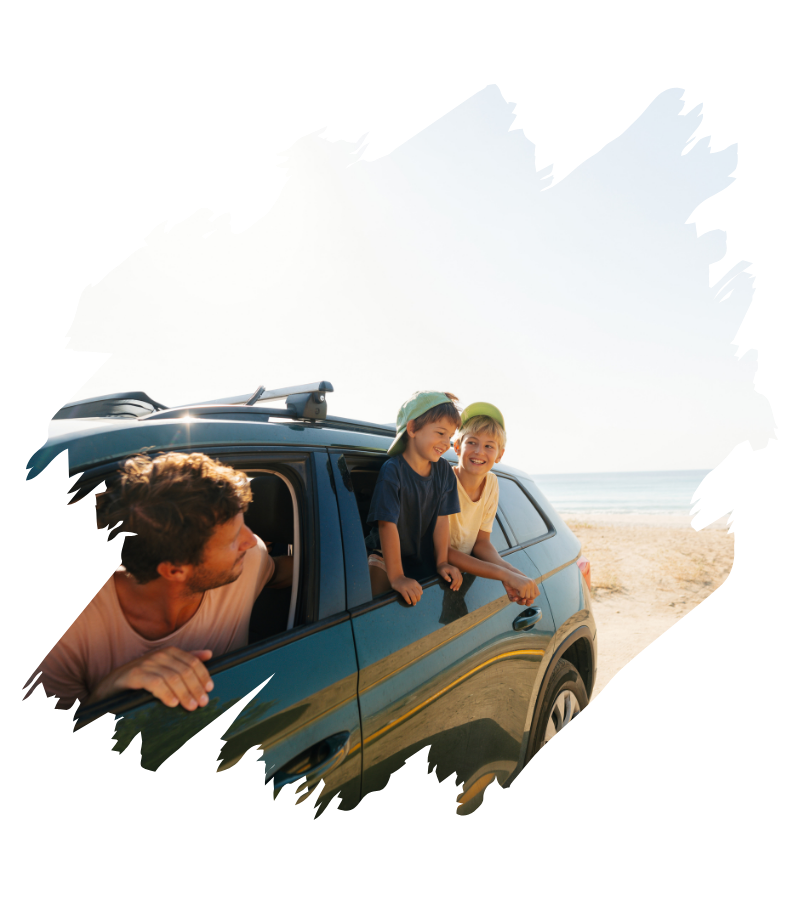 Ein Vater lehnt sich aus dem Fahrerfenster eines SUV, während zwei Kinder fröhlich am Strand aus dem Auto schauen und lachen.