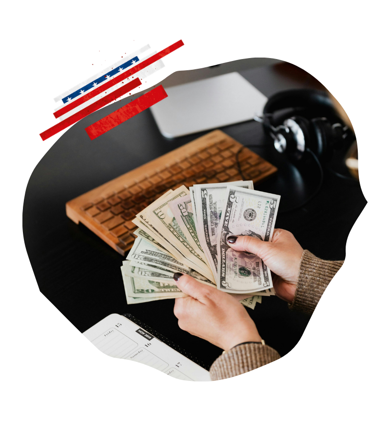 US-Dollar werden am Schreibtisch neben einer Tastatur gezählt, während eine Kreditkarte für Zahlungen bei USA-Reisen bereitliegt.