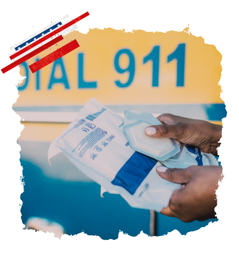 Hände halten in den USA einen Notfallverband vor dem Schriftzug DIAL 911, während die Nummer für Polizei, Feuerwehr und Rettungsdienst im Hintergrund steht.