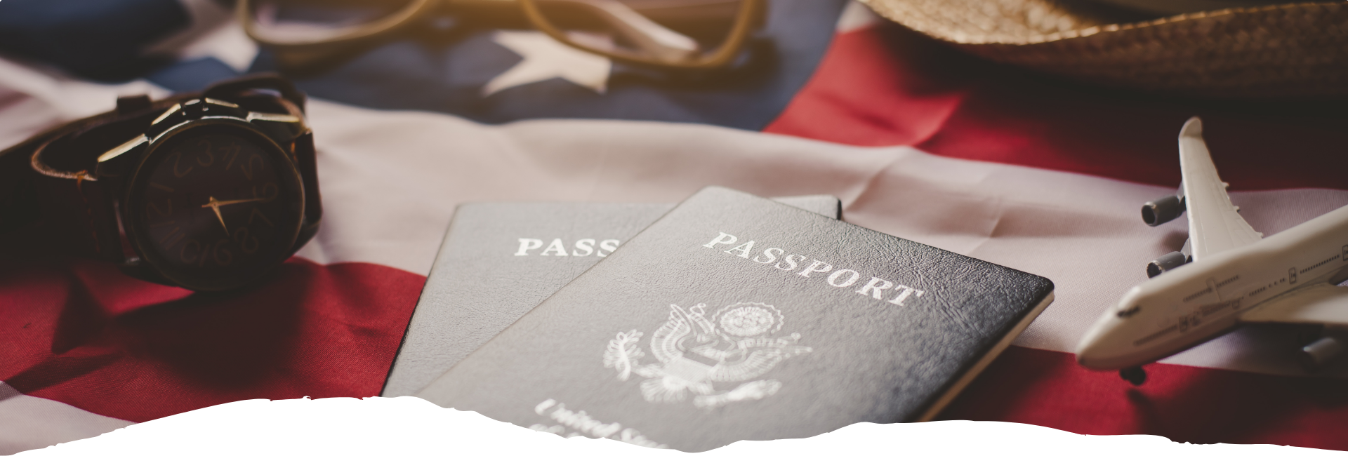 Auf dem rot-weißen Hintergrund liegen zwei Reisepässe neben einem Modellflugzeug und einer Armbanduhr, passend zum Thema USA-Einreise.