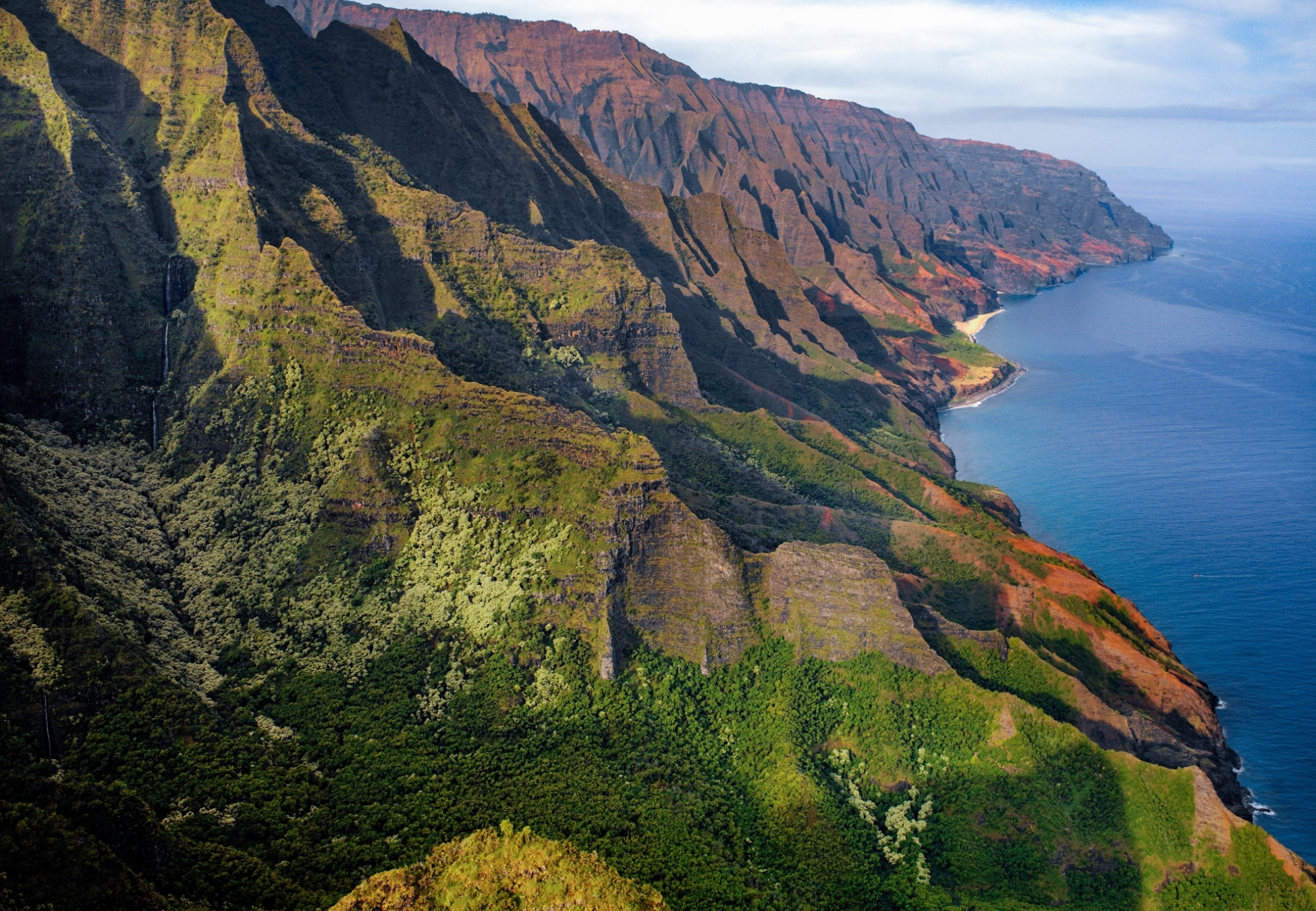 Grüne, steile Küstenklippen auf Hawaii fallen zum tiefblauen Meer an der Nā Pali Coast ab.