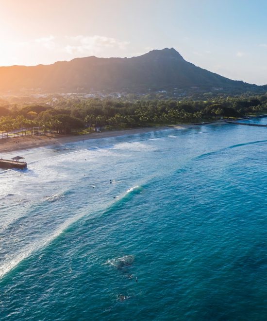 Die Waikīkī-Bucht auf Oʻahu liegt vor Diamond Head, mit türkisblauem Wasser, Sandstrand und Küstenhotels im warmen Licht.