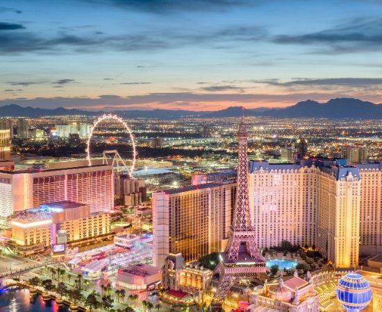 Las Vegas leuchtet bei Sonnenuntergang mit dem High Roller, der Eiffel Tower-Attrappe und der Skyline am Strip.