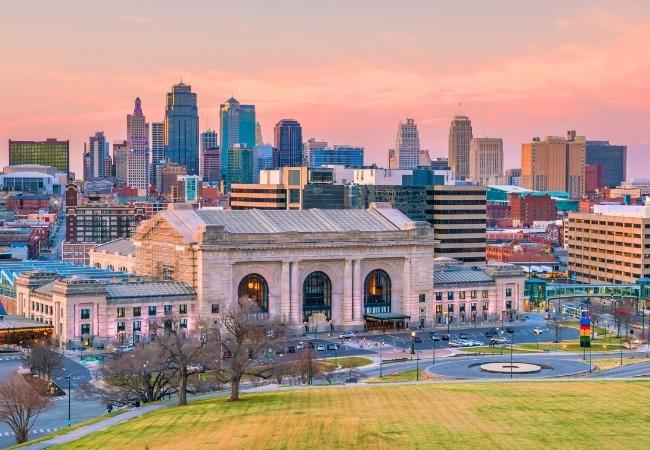 Die Union Station von Kansas City steht vor der Skyline der Stadt unter einem rosa Abendhimmel.