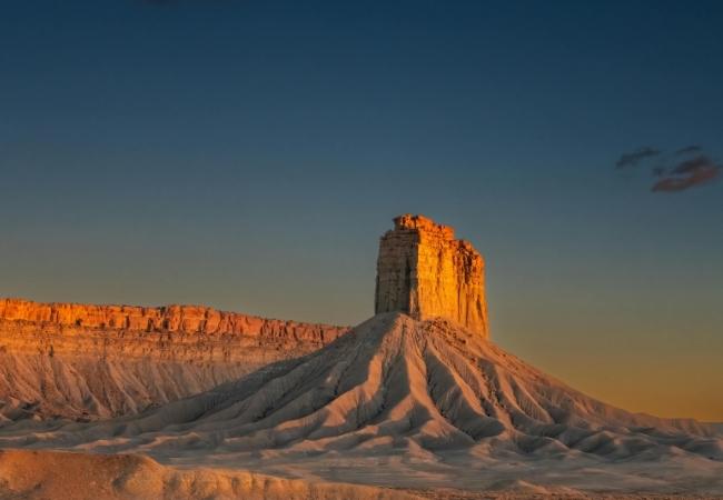 Der Devils Tower erhebt sich in warmem Licht über hellen, zerfurchten Felsformationen unter klarem Abendhimmel.