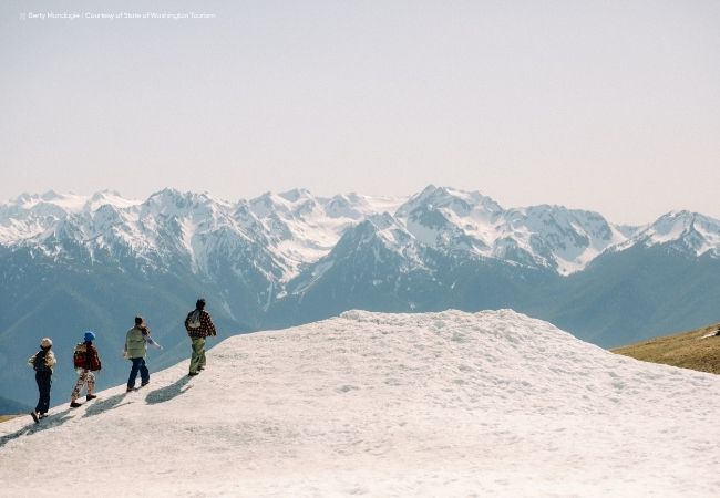 Vier Wanderer stehen auf einem verschneiten Hang vor schroffen, schneebedeckten Berggipfeln im Pacific Northwest.