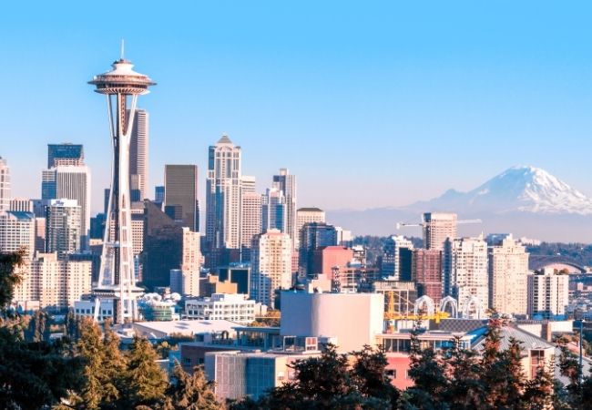 Die Skyline von Seattle mit der Space Needle im Vordergrund und Mount Rainier im Hintergrund unter klarem Himmel.