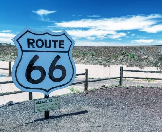 Das Route-66-Schild in Williams, Arizona steht vor weitem Himmel mit lockeren Wolken und markiert die historische Strecke.