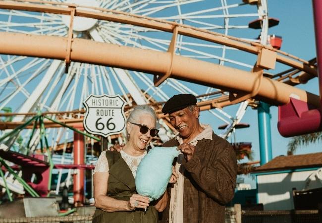 Ein lachendes Paar hält Zuckerwatte vor einem Riesenrad, daneben steht das Schild „Historic Route 66“.