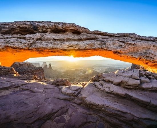 Unter einem natürlichen Felsbogen in Arizona fällt Sonnenlicht auf die steinige Landschaft des Südwestens bei klarer Sicht.