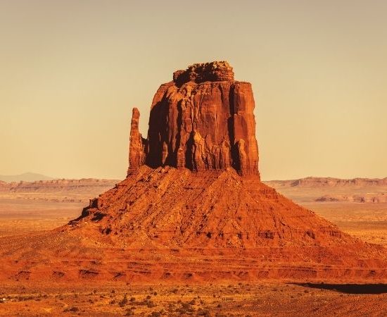 Eine mächtige rote Felsformation erhebt sich in der weiten Wüstenlandschaft von Monument Valley in Arizona.