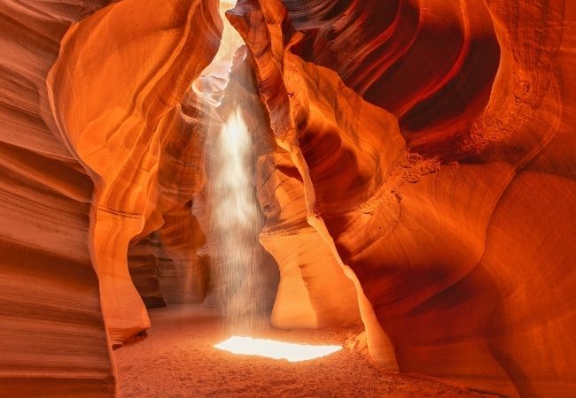 Ein Lichtstrahl fällt durch die enge Sandsteinschlucht des Antelope Canyon in Arizona und beleuchtet die roten Felswände.