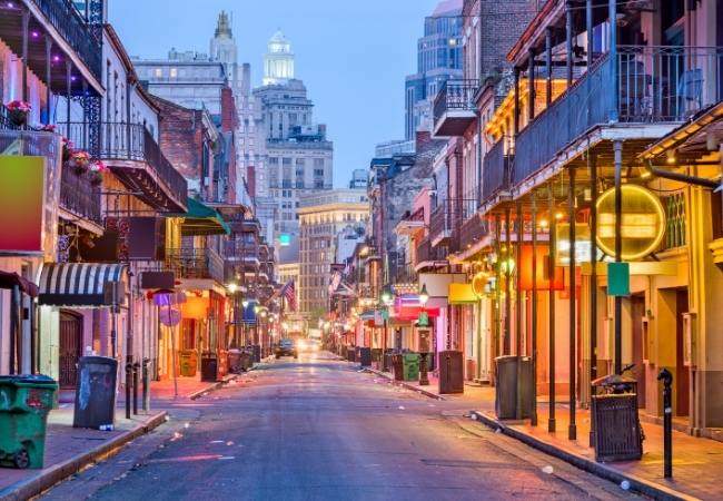 Eine leere Straße mit historischen Balkonen und warm beleuchteten Fassaden in der Altstadt von New Orleans bei Dämmerung.