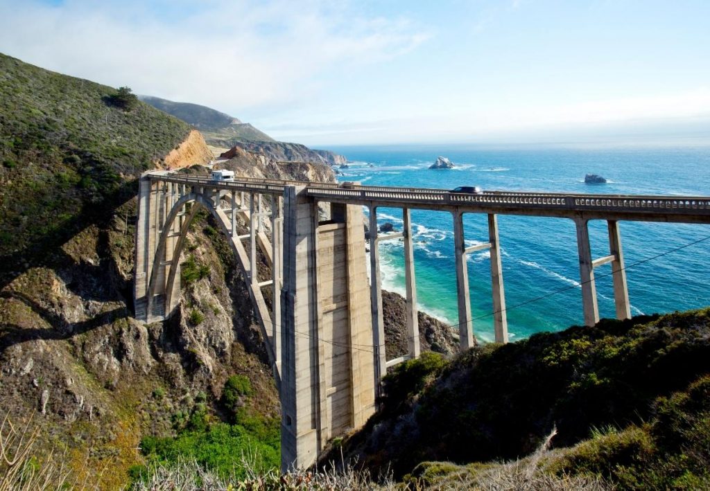 Die Bixby Creek Bridge spannt sich über steile Klippen in Big Sur, darunter glitzert der Pazifik in hellem Blau.