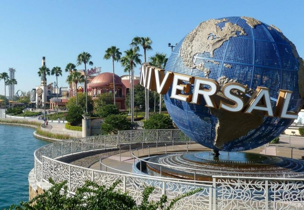 Der blaue Universal-Globus steht am Wasser vor Palmen und Parkgebäuden bei klarem Himmel in Los Angeles.