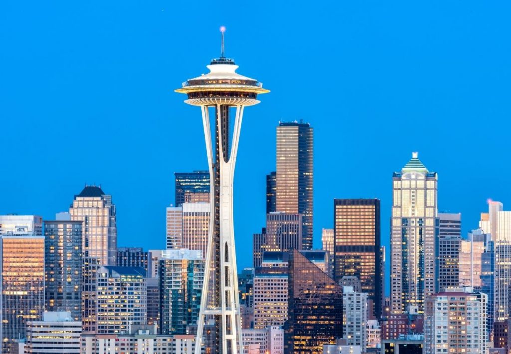 Die Space Needle ragt über die beleuchtete Skyline von Seattle unter einem klaren blauen Abendhimmel.