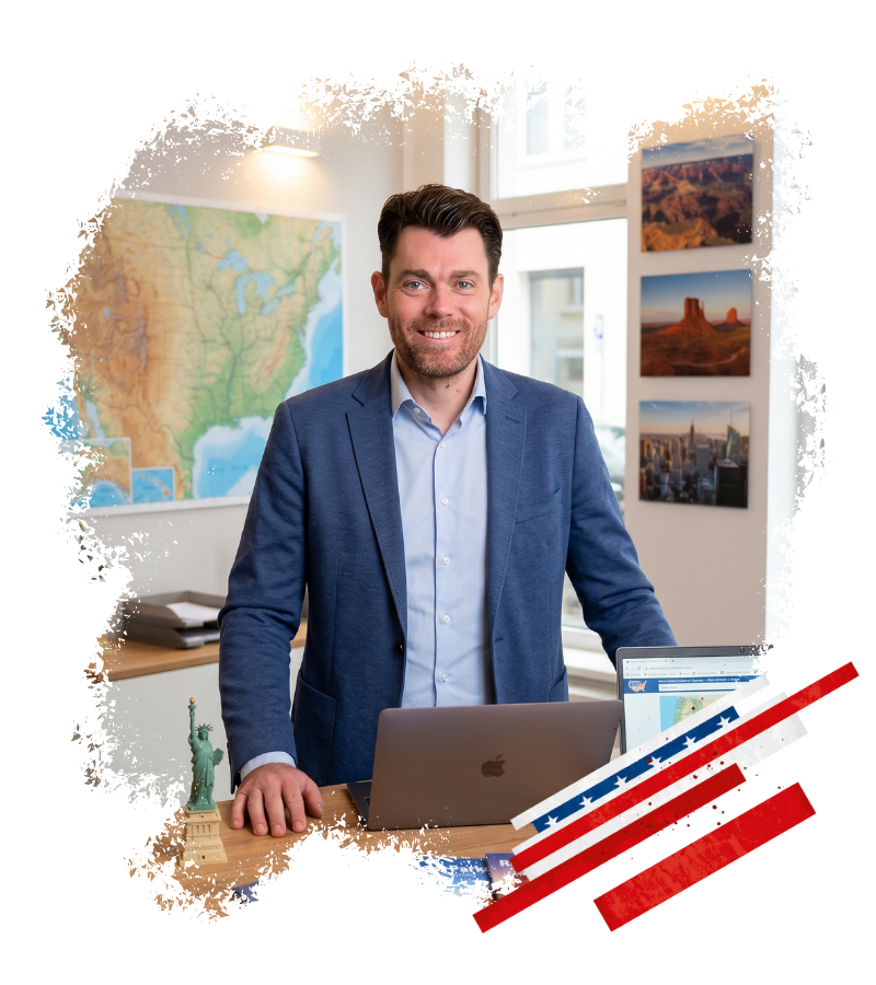 David steht im Büro von USA-Reisen-Experte vor Laptop und USA-Karte, umgeben von Bildern westamerikanischer Landschaften.
