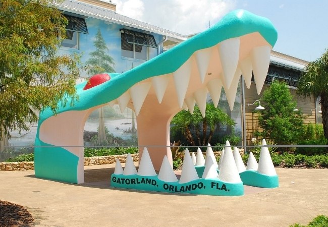 Vor dem Eingang von Gatorland in Orlando steht eine türkis-weiße Krokodilmaul-Skulptur mit großen Zähnen und dem Schriftzug Gatorland, Orlando, Fla.