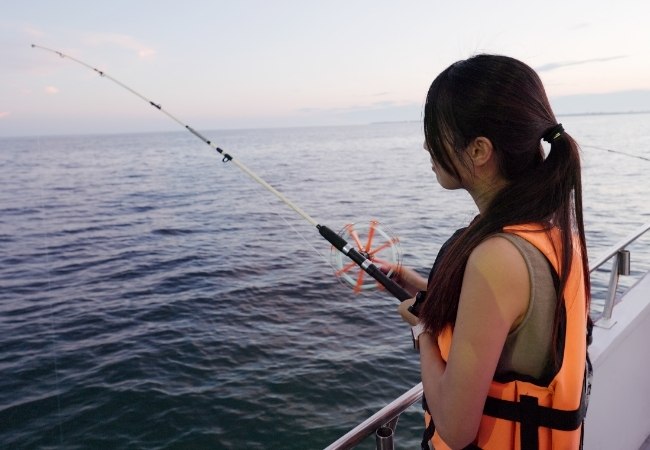 Eine Anglerin im orangefarbenen Rettungswesten hält die Angel an Bord eines Bootes vor Florida, während die ruhige See im Abendlicht am offenen Meer liegt.