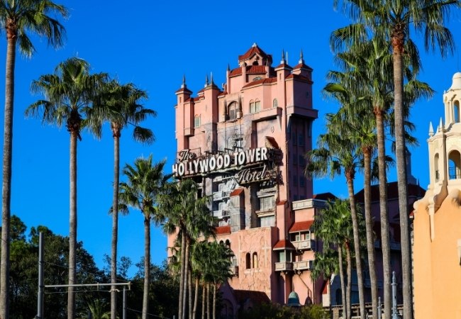 Die Hollywood Tower Hotel-Fassade in den Disney's Hollywood Studios steht zwischen hohen Palmen unter wolkenlosem Himmel in Orlando, Florida.